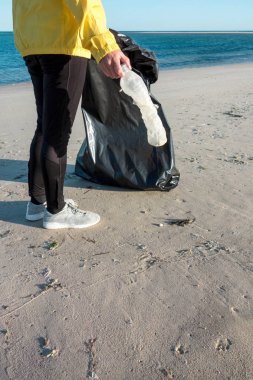 Çöp ve plastik toplayan kadın çöp torbasıyla plajı temizliyor. İklim değişikliği ve okyanusların kirliliğine karşı çevre gönüllü aktivisti.