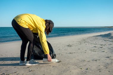 Çöp ve plastik toplayan kadın çöp torbasıyla plajı temizliyor. İklim değişikliği ve okyanusların kirliliğine karşı çevre gönüllü aktivisti.