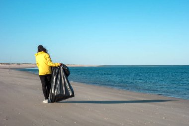 Çöp ve plastik toplayan kadın çöp torbasıyla plajı temizliyor. İklim değişikliği ve okyanusların kirliliğine karşı çevre gönüllü aktivisti.