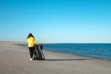 Çöp ve plastik toplayan kadın çöp torbasıyla plajı temizliyor. İklim değişikliği ve okyanusların kirliliğine karşı çevre gönüllü aktivisti.