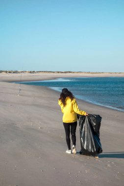 Çöp ve plastik toplayan kadın çöp torbasıyla plajı temizliyor. İklim değişikliği ve okyanusların kirliliğine karşı çevre gönüllü aktivisti.