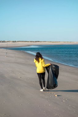 Çöp ve plastik toplayan kadın çöp torbasıyla plajı temizliyor. İklim değişikliği ve okyanusların kirliliğine karşı çevre gönüllü aktivisti.