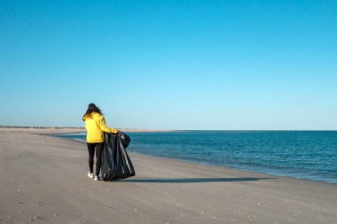 Çöp ve plastik toplayan kadın çöp torbasıyla plajı temizliyor. İklim değişikliği ve okyanusların kirliliğine karşı çevre gönüllü aktivisti.