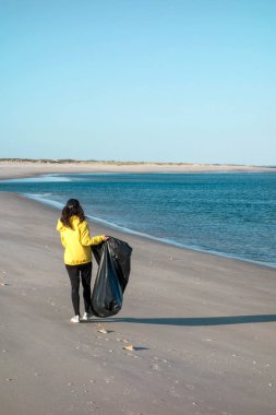 Çöp ve plastik toplayan kadın çöp torbasıyla plajı temizliyor. İklim değişikliği ve okyanusların kirliliğine karşı çevre gönüllü aktivisti.