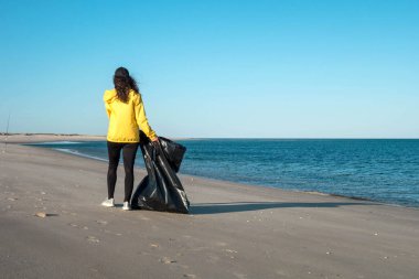 Çöp ve plastik toplayan kadın çöp torbasıyla plajı temizliyor. İklim değişikliği ve okyanusların kirliliğine karşı çevre gönüllü aktivisti.