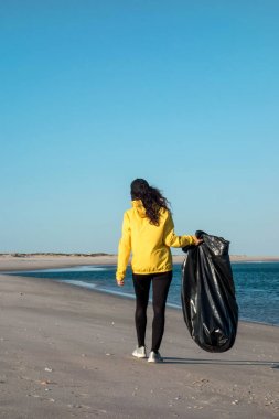 Çöp ve plastik toplayan kadın çöp torbasıyla plajı temizliyor. İklim değişikliği ve okyanusların kirliliğine karşı çevre gönüllü aktivisti.