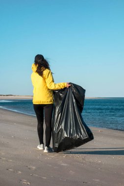 Çöp ve plastik toplayan kadın çöp torbasıyla plajı temizliyor. İklim değişikliği ve okyanusların kirliliğine karşı çevre gönüllü aktivisti.