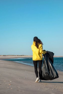 Çöp ve plastik toplayan kadın çöp torbasıyla plajı temizliyor. İklim değişikliği ve okyanusların kirliliğine karşı çevre gönüllü aktivisti.