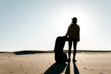 Çöp ve plastik toplayan kadın çöp torbasıyla plajı temizliyor. İklim değişikliği ve okyanusların kirliliğine karşı çevre gönüllü aktivisti.