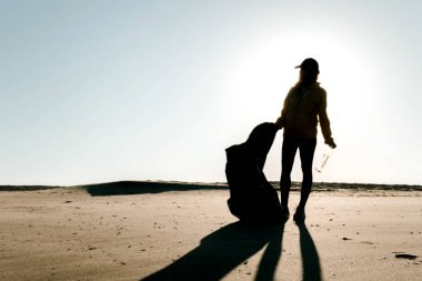 Çöp ve plastik toplayan kadın çöp torbasıyla plajı temizliyor. İklim değişikliği ve okyanusların kirliliğine karşı çevre gönüllü aktivisti.