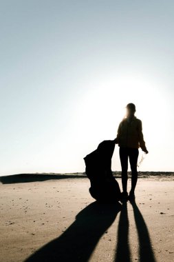 Çöp ve plastik toplayan kadın çöp torbasıyla plajı temizliyor. İklim değişikliği ve okyanusların kirliliğine karşı çevre gönüllü aktivisti.