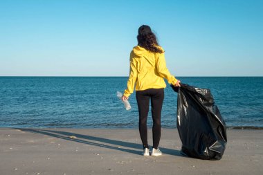 Çöp ve plastik toplayan kadın çöp torbasıyla plajı temizliyor. İklim değişikliği ve okyanusların kirliliğine karşı çevre gönüllü aktivisti.