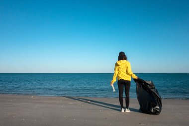 Çöp ve plastik toplayan kadın çöp torbasıyla plajı temizliyor. İklim değişikliği ve okyanusların kirliliğine karşı çevre gönüllü aktivisti.