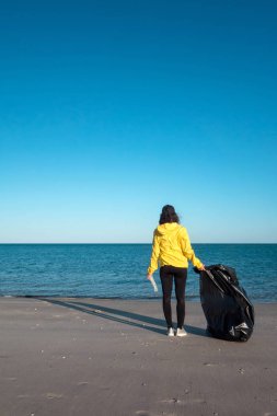 Çöp ve plastik toplayan kadın çöp torbasıyla plajı temizliyor. İklim değişikliği ve okyanusların kirliliğine karşı çevre gönüllü aktivisti.