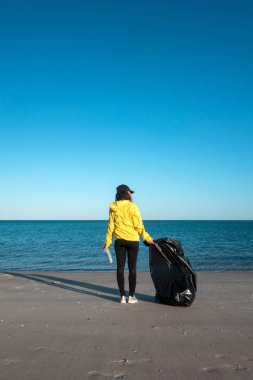 Çöp ve plastik toplayan kadın çöp torbasıyla plajı temizliyor. İklim değişikliği ve okyanusların kirliliğine karşı çevre gönüllü aktivisti.