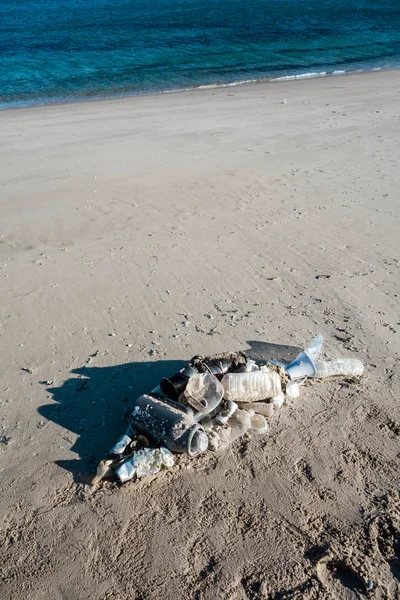 Fish shape laying on beach sand made of ocean trash. Plastic pollution concept.