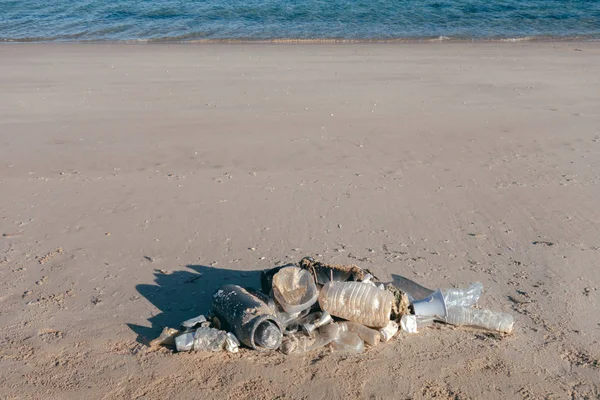 Fish shape laying on beach sand made of ocean trash. Plastic pollution concept.