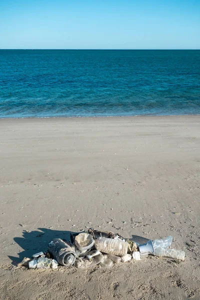 Fish shape laying on beach sand made of ocean trash. Plastic pollution concept.