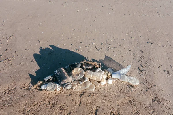 Fish shape laying on beach sand made of ocean trash. Plastic pollution concept.