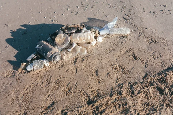 Fish shape laying on beach sand made of ocean trash. Plastic pollution concept.