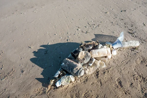 Fish shape laying on beach sand made of ocean trash. Plastic pollution concept.