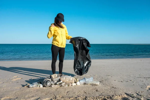 Çöp ve plastik toplayan kadın çöp torbasıyla plajı temizliyor. İklim değişikliği ve okyanusların kirliliğine karşı çevre gönüllü aktivisti.