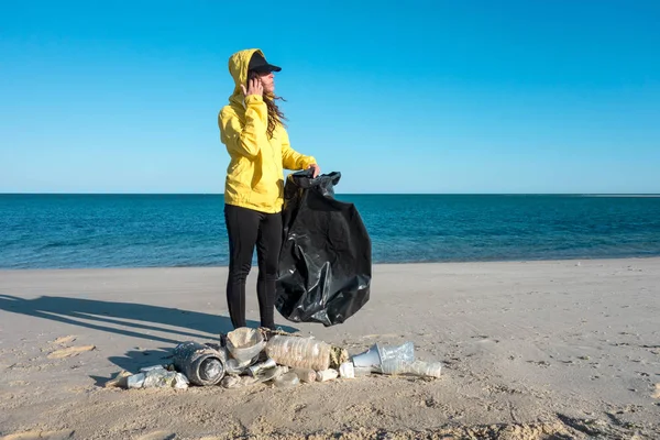 Çöp ve plastik toplayan kadın çöp torbasıyla plajı temizliyor. İklim değişikliği ve okyanusların kirliliğine karşı çevre gönüllü aktivisti.