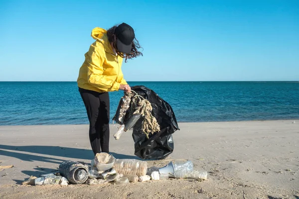Çöp ve plastik toplayan kadın çöp torbasıyla plajı temizliyor. İklim değişikliği ve okyanusların kirliliğine karşı çevre gönüllü aktivisti.