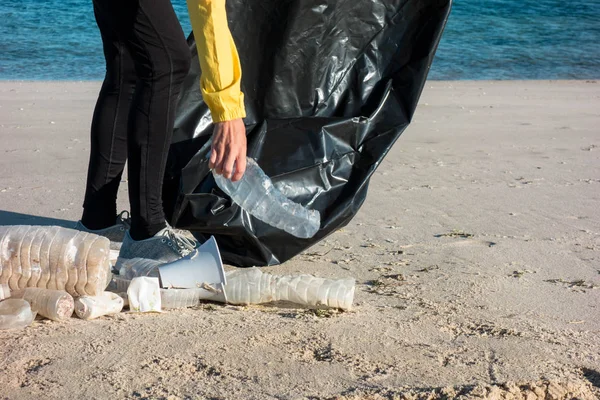 Çöp ve plastik toplayan kadın çöp torbasıyla plajı temizliyor. İklim değişikliği ve okyanusların kirliliğine karşı çevre gönüllü aktivisti.