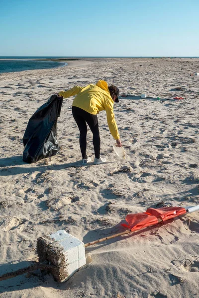 Çöp ve plastik toplayan kadın çöp torbasıyla plajı temizliyor. İklim değişikliği ve okyanusların kirliliğine karşı çevre gönüllü aktivisti.