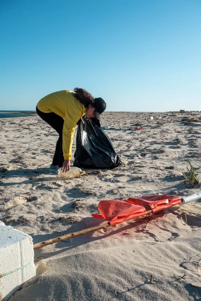 Çöp ve plastik toplayan kadın çöp torbasıyla plajı temizliyor. İklim değişikliği ve okyanusların kirliliğine karşı çevre gönüllü aktivisti.