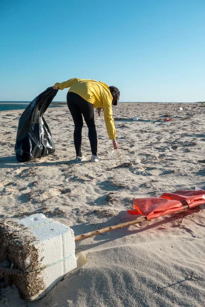 Çöp ve plastik toplayan kadın çöp torbasıyla plajı temizliyor. İklim değişikliği ve okyanusların kirliliğine karşı çevre gönüllü aktivisti.