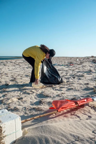 Woman picking up trash and plastics cleaning the beach with a garbage bag. Environmental volunteer activist against climate change and the pollution of the oceans.