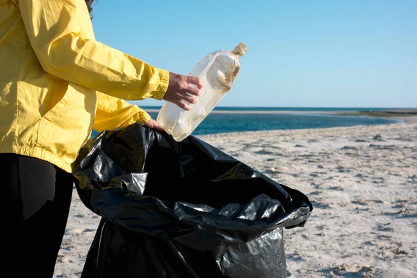 Çöp ve plastik toplayan kadın çöp torbasıyla plajı temizliyor. İklim değişikliği ve okyanusların kirliliğine karşı çevre gönüllü aktivisti.