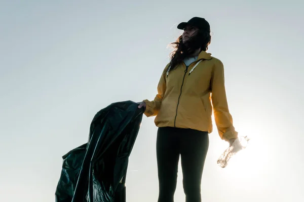 Woman picking up trash and plastics cleaning the beach with a garbage bag. Environmental volunteer activist against climate change and the pollution of the oceans.