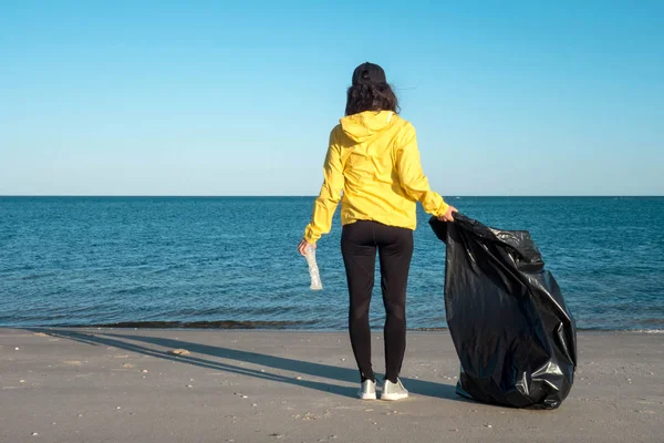 Çöp ve plastik toplayan kadın çöp torbasıyla plajı temizliyor. İklim değişikliği ve okyanusların kirliliğine karşı çevre gönüllü aktivisti.