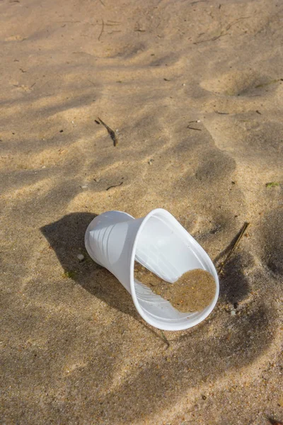 Plastic cup on the beach sand. Plastic pollution of the oceans concept.