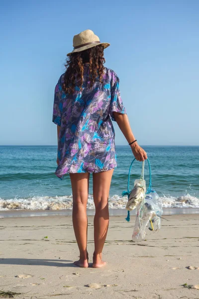 Woman picking up trash and plastics cleaning the beach. Environmental volunteer activist against climate change and the pollution of the oceans.