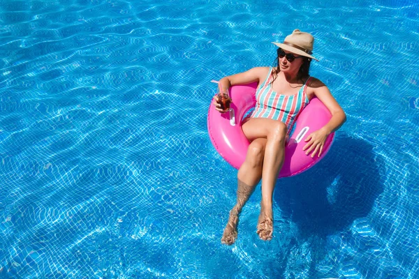 파란색 수영장에서 선글라스 모자와 수영복을 칵테일을 마시면서 여름을 즐기는 분홍색 — 스톡 사진