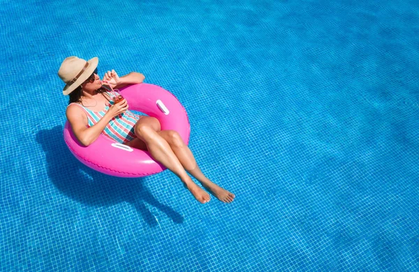 파란색 수영장에서 선글라스 모자와 수영복을 칵테일을 마시면서 여름을 즐기는 분홍색 — 스톡 사진
