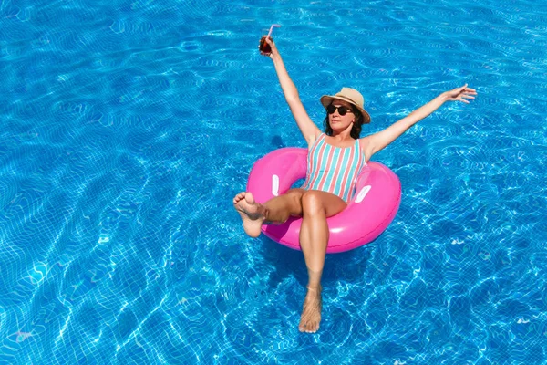 青いプールにサングラス 水着を着た若い女性 カクテルを飲みながら 開いた腕で夏を楽しむピンクのフロートのかわいい女の子 — ストック写真