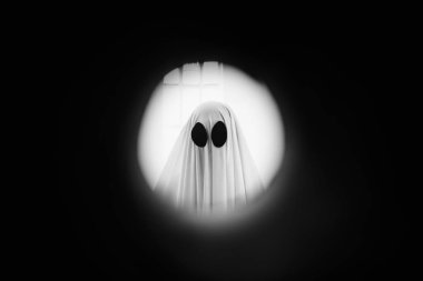 Hayalet, kapının arkasındaki gözetleme deliğinden beyaz bir hayalet örtüsüyle kaplanmış. Cadılar Bayramı Konsepti