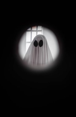 Hayalet, kapının arkasındaki gözetleme deliğinden beyaz bir hayalet örtüsüyle kaplanmış. Cadılar Bayramı Konsepti