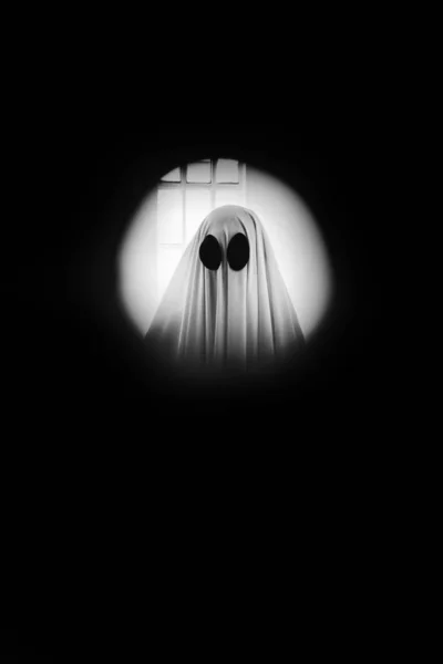 鬼魂透过窥探孔 在门后面盖着一张白色的鬼片 万圣节概念 — 图库照片