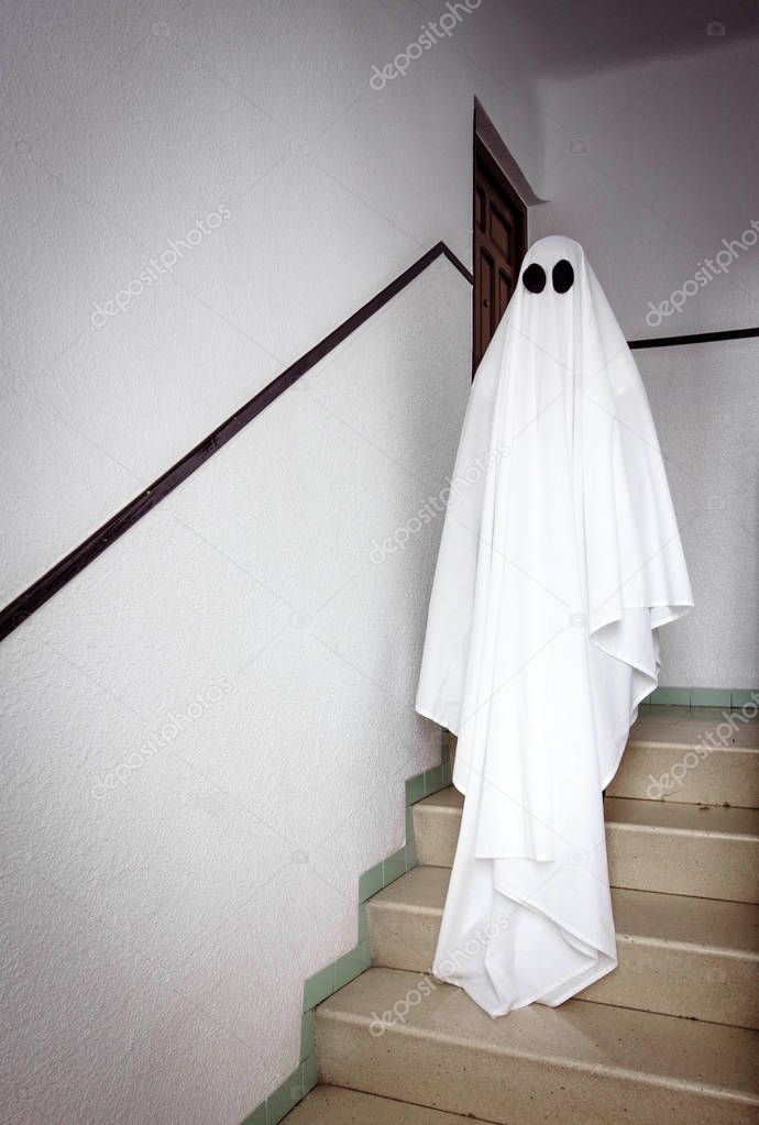 Ghost covered with a white ghost sheet on the stairs of an abandoned psychiatric hospital. Halloween Concept