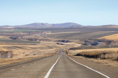 Ufuk düzgün tepelerin arasında asfalt yol ile sonbahar manzara kuru sarı çim kaplı ve tarım alanları Khakassia, Rusya'da temizlenmesi
