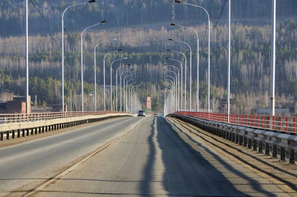 Perspective view on asphalt road on river bridge with lamp posts in Siberia, Russia