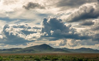 Khakassia, Sibirya, Rusya'da güneş ışığı ışınları ile gün batımı sırasında ağır bulutlar gökyüzü altında bozkırda ufukta çim tepeler.