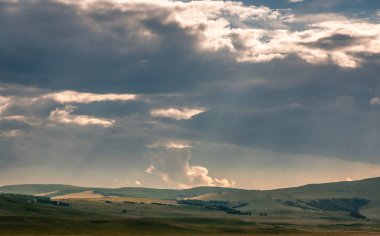 Khakassia, Sibirya, Rusya'da güneş ışığı ışınları ile gün batımı sırasında ağır bulutlar gökyüzü altında bozkırda ufukta çim tepeler.