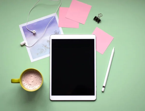 Yeşil bir arka plan bir kalemi ile tablet. Bir fincan kahve, kulaklık, fotoğraf. Yaşam tarzı